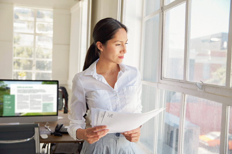 Person looking out window holding paper prints